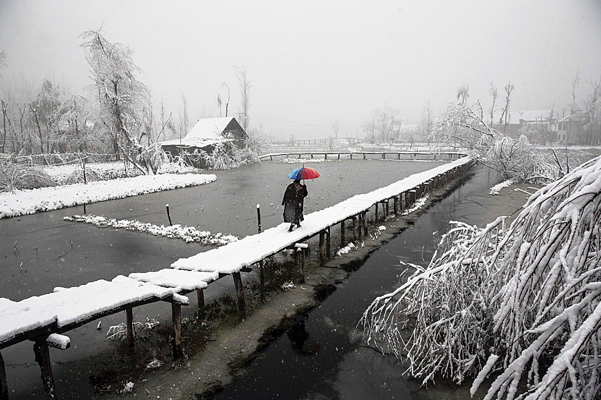 A Kashmiri walks on a snow-covered footbridge as it snows in the interiors of Dal Lake in Srinagar on December 13, 2019.