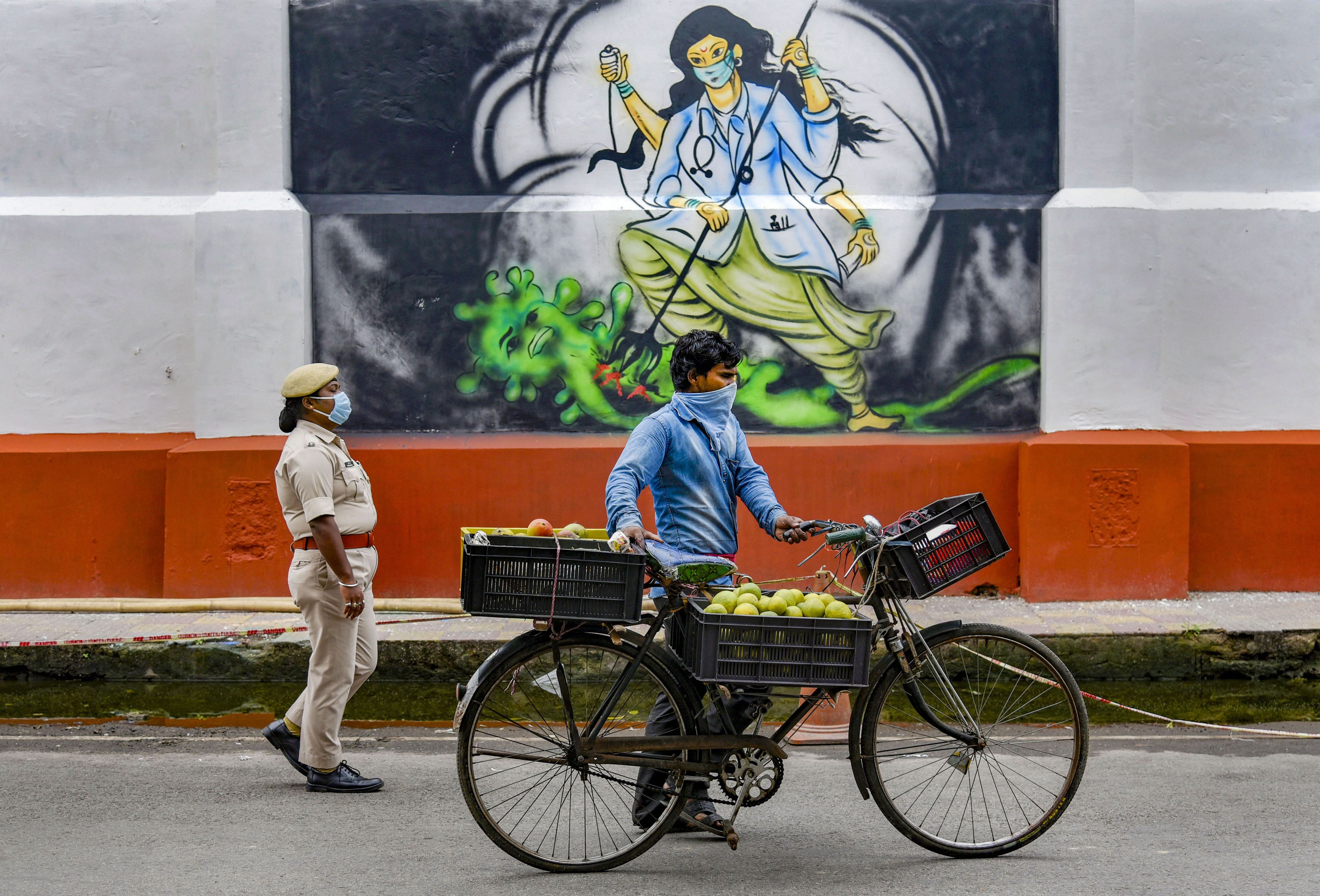 A fruit vendor and a police personnel walk past a mural that glorifies medical workers, during the ongoing Covid-19 nationwide lockdown, in Guwahati, Wednesday, May 6, 2020