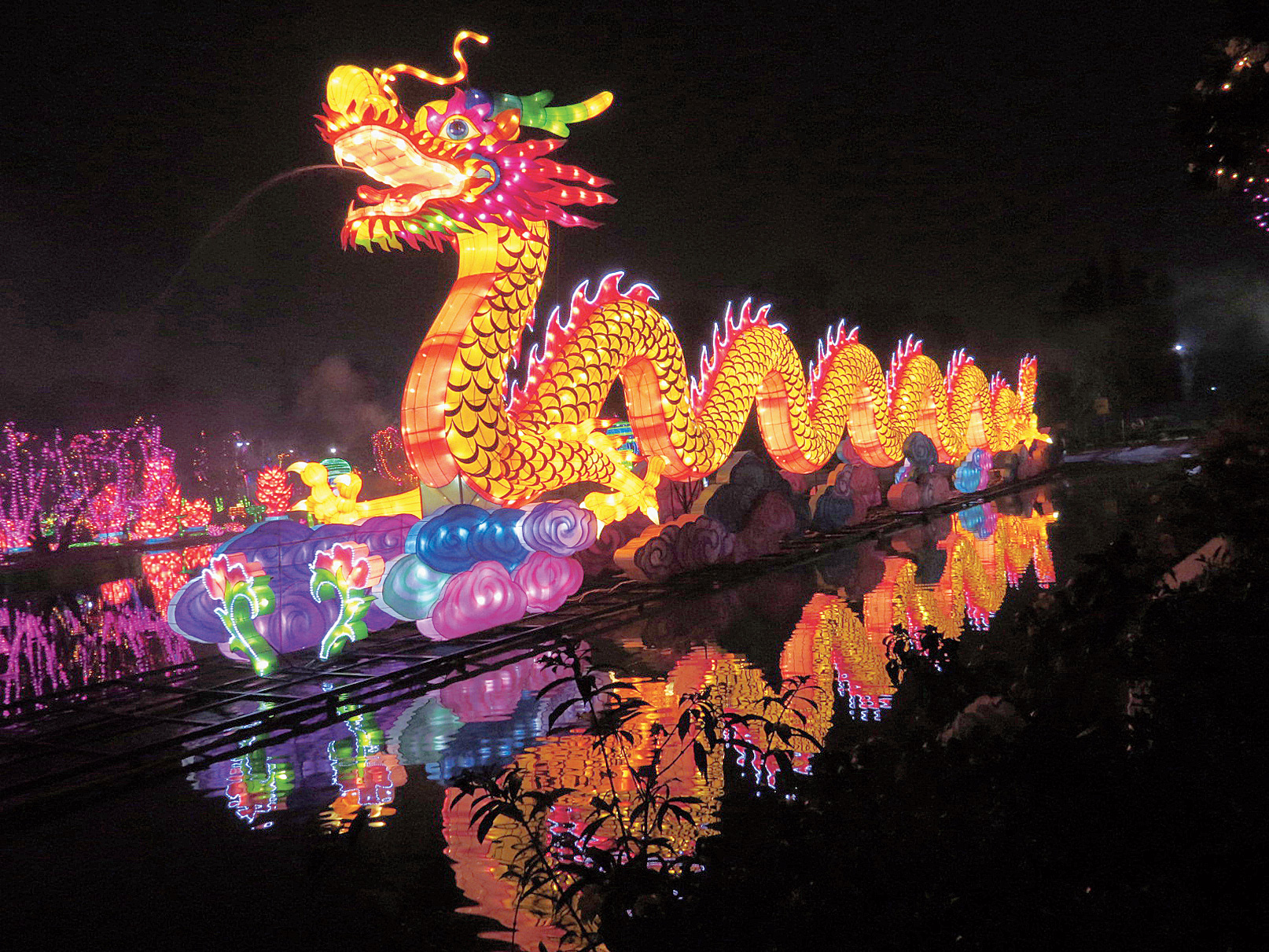 A yellow dragon reflected in the lake as it spews a jet of water.