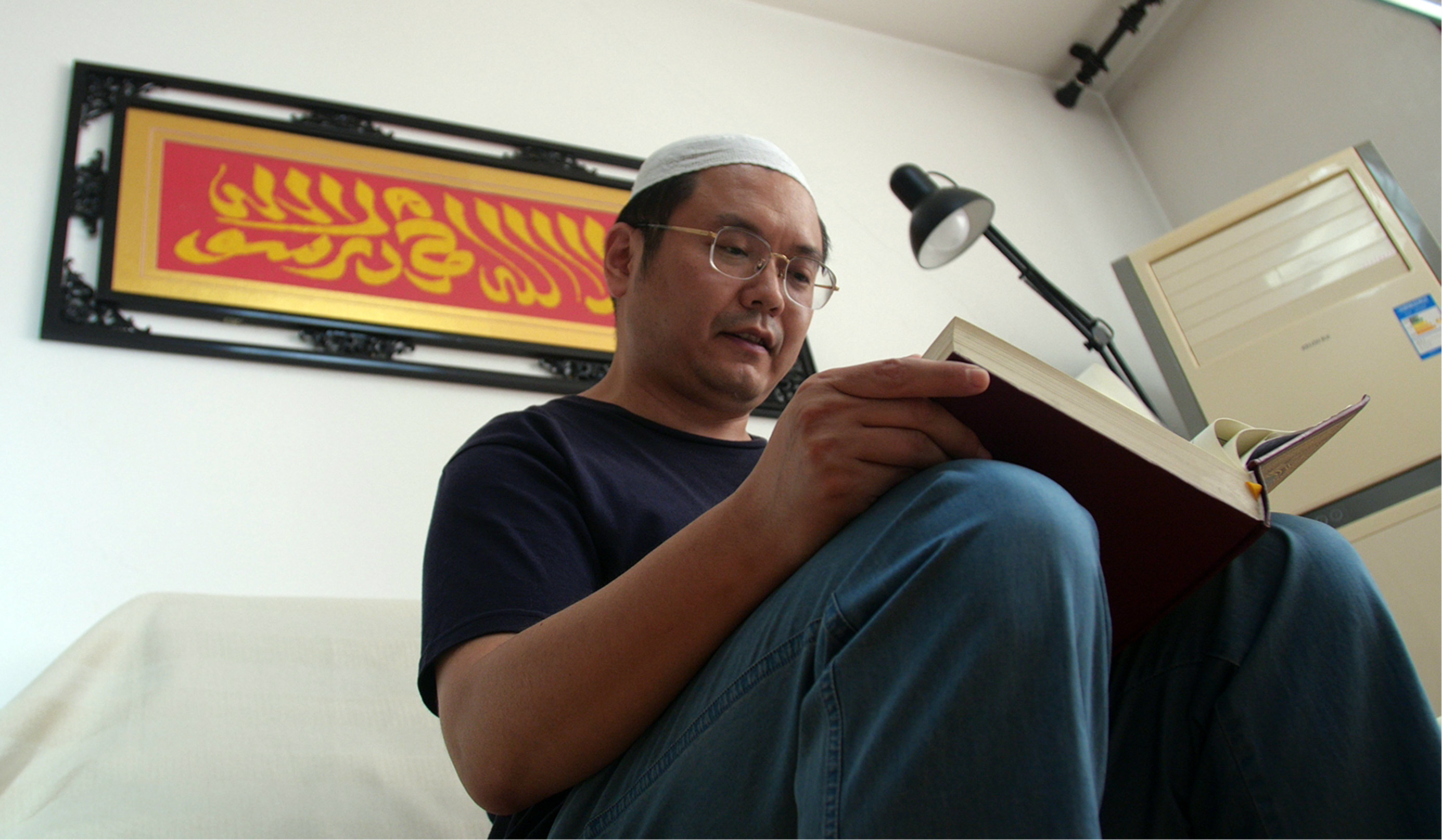 Cui Haoxin reads an Arabic prayer from the Quran in his home in Jinan in China's eastern province of Shandong. Behind him is a tapestry woven by his mother, which reads in Arabic: 