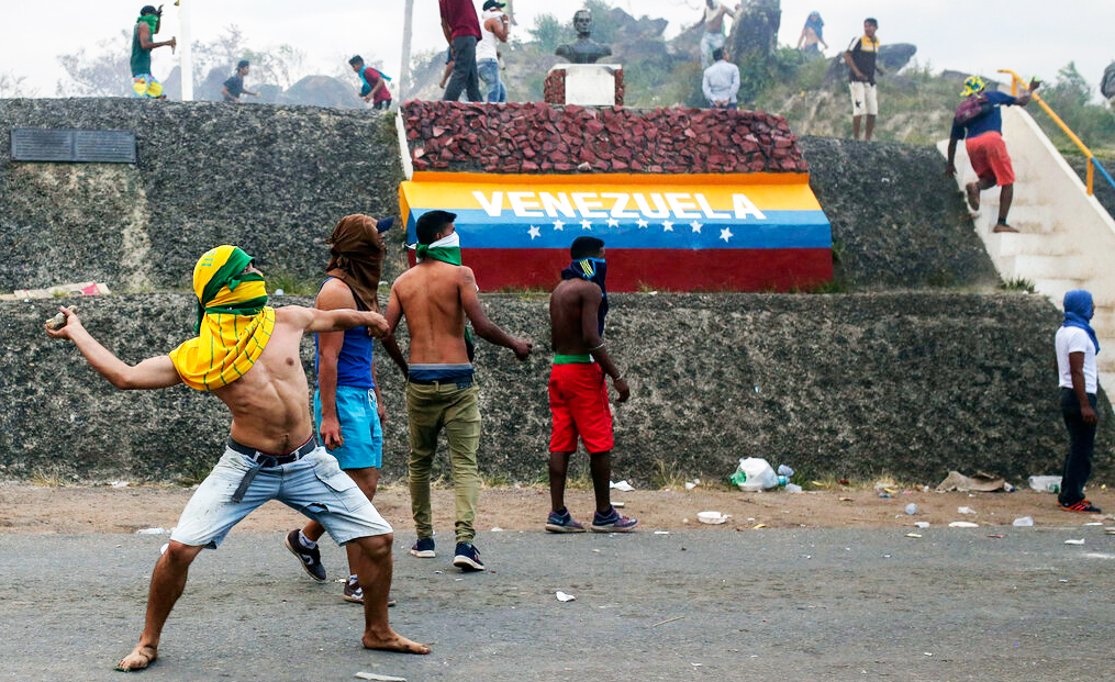 Venezuelan demonstrators throw stones during clashes with authorities, at the border between Brazil and Venezuela on Saturday, Feb.23, 2019. 