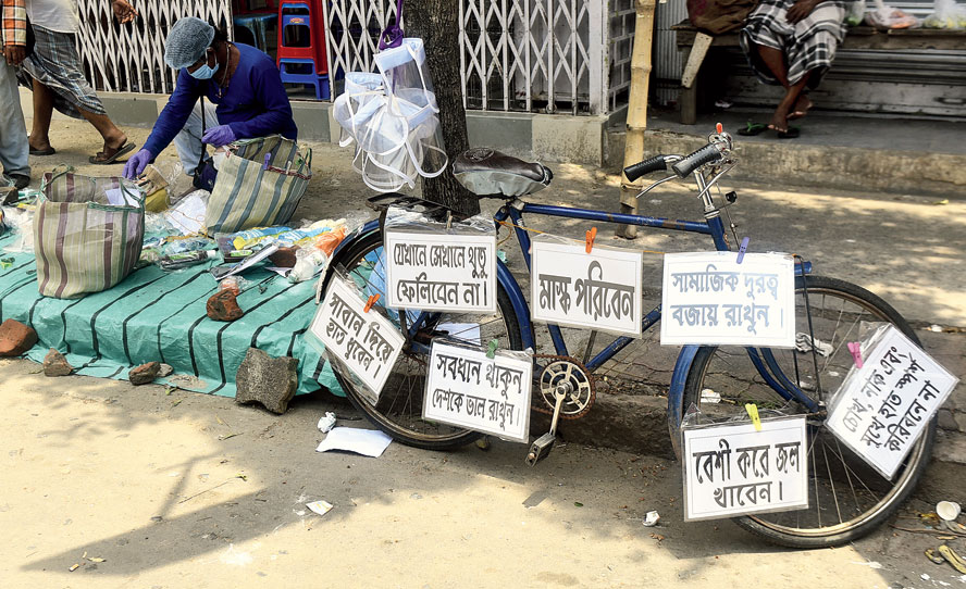 A man sitting on a sidewalk along Dum Dum Road, near the railway station, with a tray full of masks, plastic face shields and hand sanitisers.