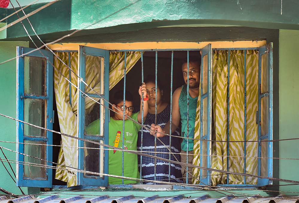 A family looks from the window of a house during the nationwide lockdown imposed to contain the coronavirus pandemic, in Calcutta, Tuesday, March 31, 2020. 