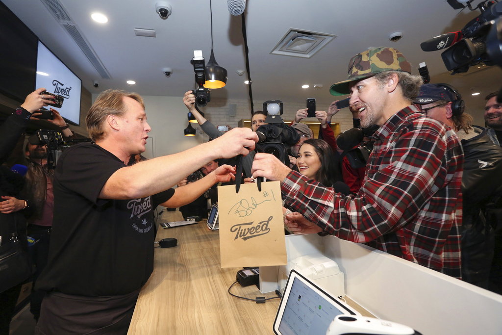 Canopy Growth CEO Bruce Linton (left) passes a bag with the first legal cannabis for recreation use sold in Canada to Nikki Rose and Ian Power.