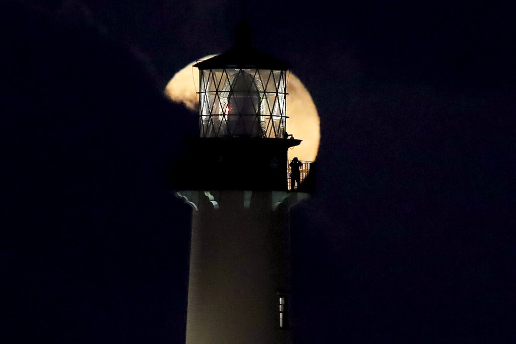 A person standing on the platform of the Jupiter Lighthouse looks at the supermoon as it is partially obscured by a cloud, Monday, March 9, 2020, in Jupiter, Florida. The 108-foot, brick lighthouse was first lit in 1860.