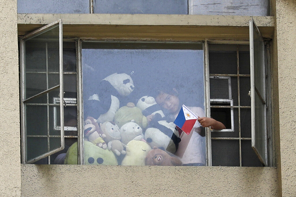 A girl waves a Philippine flag beside stuff toys as residents clap and sing from their windows to pay tribute to health workers, essential personnel and security forces during an enhanced community quarantine to prevent the spread of the new coronavirus in Manila, Philippines, Sunday, April 12, 2020.