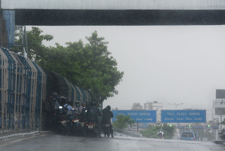 Storm cover: Bikers take shelter from the rain under the Vidyasagar Setu around 11am on Saturday.