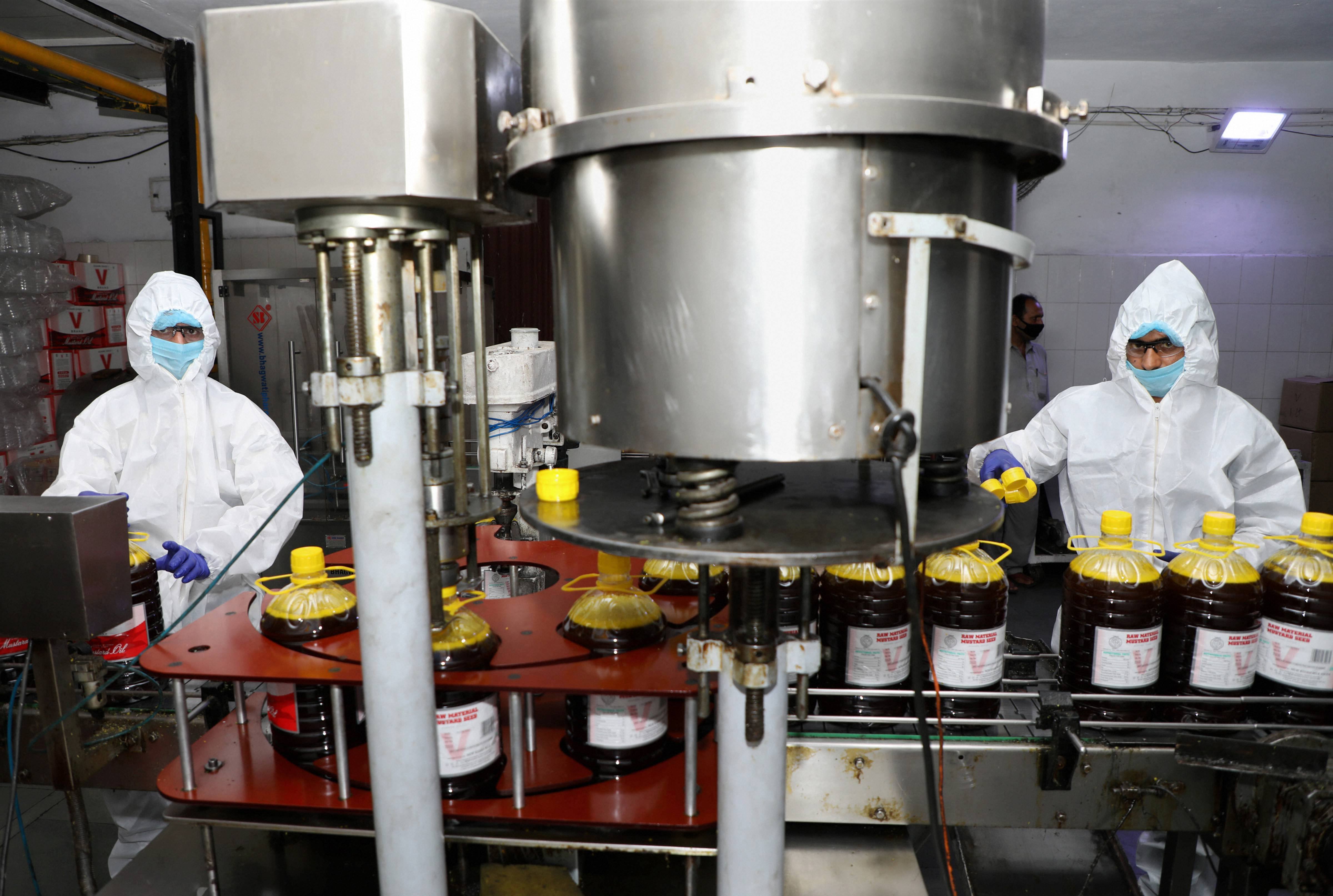 Workers wearing protective suits work at a machine packing edible oil at a factory, during the ongoing Covid-19 lockdown, in Jammu, Tuesday, May 19, 2020.